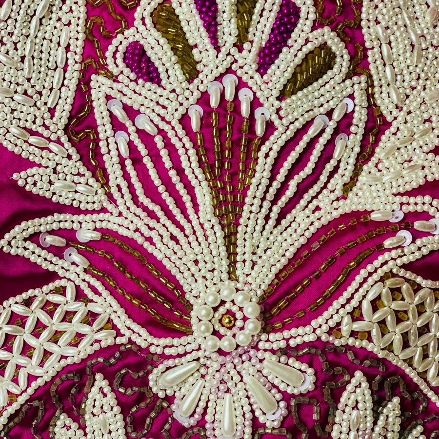 Detail perlové a zlaté výšivky na purpurovém hedvábí